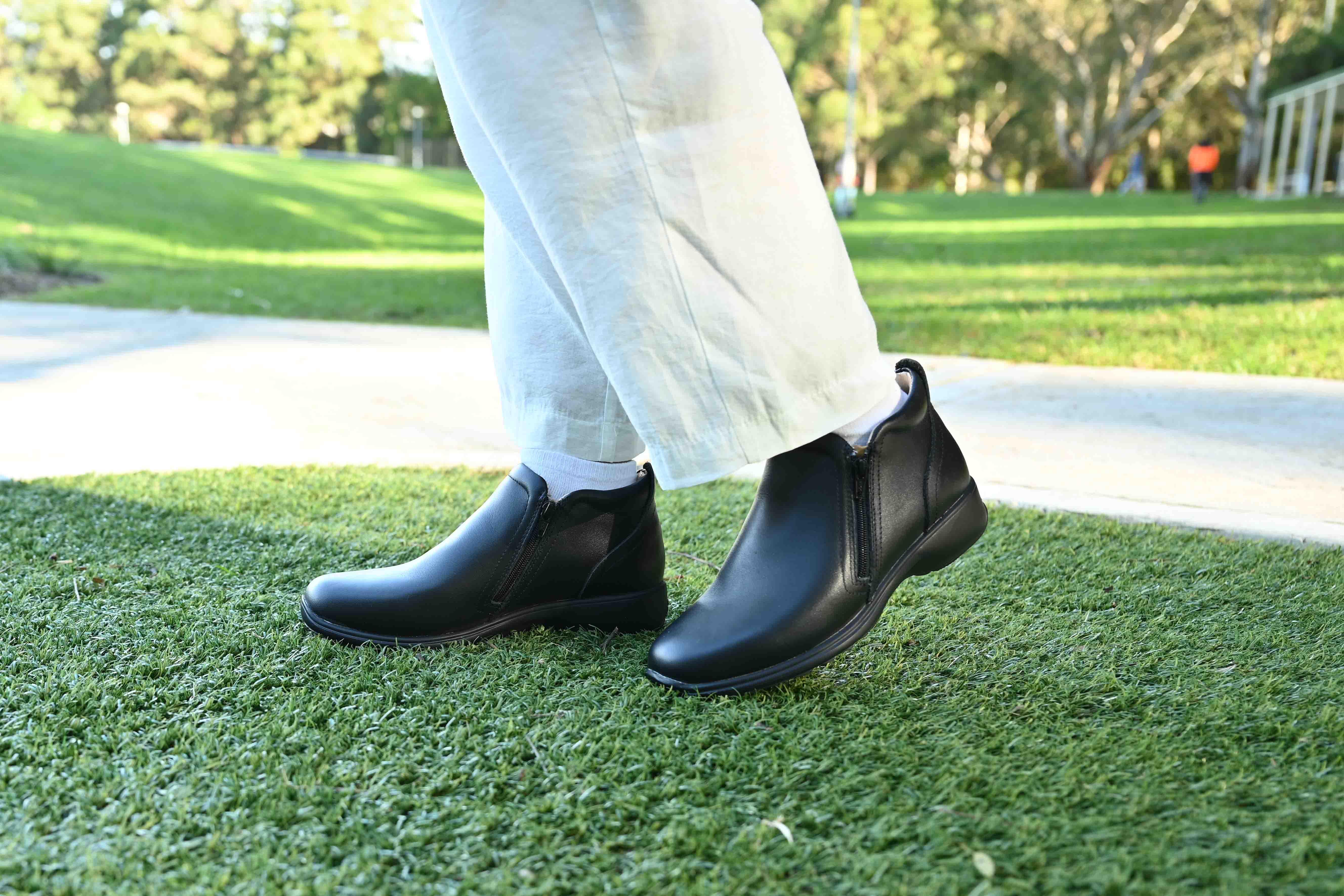 Person wearing black leather ankle boots and white pants outdoors on grass
